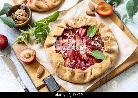 Plum Galette. Gesunder hausgemachter Vollkornfruchtkuchen (Galette) mit Pflaumen und Mandeln, veganes vegetarisches Dessert auf einem Steintisch. Stockfoto