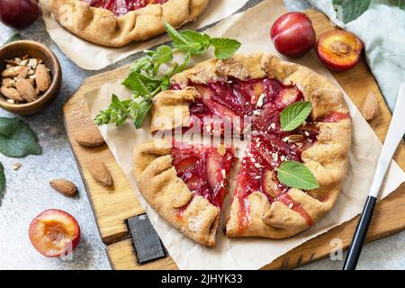 Plum Galette. Gesunder hausgemachter Vollkornfruchtkuchen (Galette) mit Pflaumen und Mandeln, veganes vegetarisches Dessert auf einem Steintisch. Stockfoto