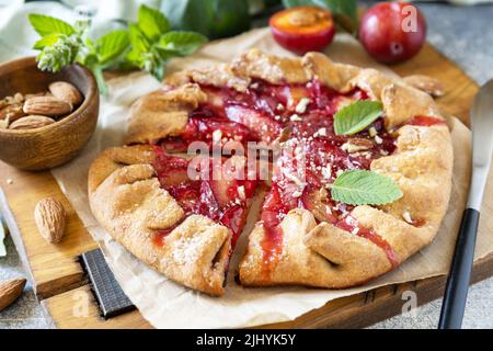 Plum Galette. Gesunder hausgemachter Vollkornfruchtkuchen (Galette) mit Pflaumen und Mandeln, veganes vegetarisches Dessert auf einem Steintisch. Stockfoto