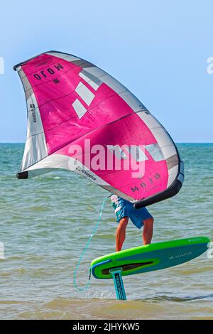 Wing Foiling / Wing Surfing an der Nordsee zeigt Wingboarder / Wing Boarder stehen auf Foilboard / Tragflügelbrett und halten einen aufblasbaren Flügel Stockfoto