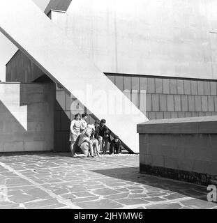 1969, historisch, außen, Liverpool Metropolitan Cathedral, Liverpool, England, Großbritannien, Studenten, die Spaß haben. Entworfen von Sir Frederick Gibberd - im modernen Stil der Ära - und aus Beton mit einer portland-Steinverkleidung gebaut, wurde es 1967 eröffnet (geweiht). Die konische Form der Kathedrale wird von riesigen Betonträgern getragen, die von zwei Ringträgern zusammengehalten werden. Stockfoto