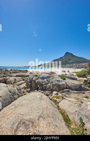 Lebhafter Strand in der Nähe von felsigen Küsten und Bergen auf blauem Himmel Hintergrund mit Kopierfläche. Heller Sommer mit Touristen unter der Sonne bräunen und genießen Stockfoto