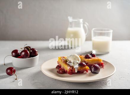 Hausgemachter süßer Kirschkuchen oder roter Brownie-Kuchen. Ein Stück mit Eis auf dem Teller, Milch und rohen Kirschen zur Seite Stockfoto