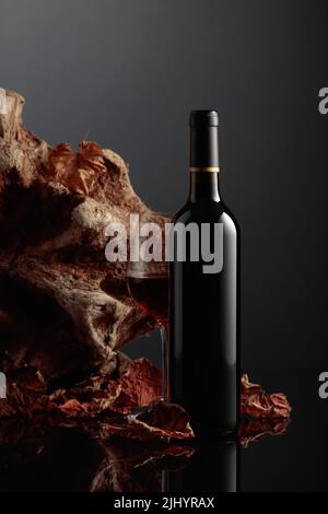 Flasche Rotwein. Im Hintergrund altes Treibholz und ausgetrocknete Weinblätter. Frontalansicht mit Platz für Ihren Text. Stockfoto