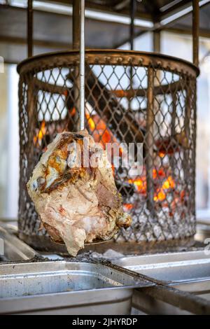 Gegrillter Schweineschinken über einem Holzfeuer. Drehbare vertikale Rotisserie Grill bbq für Street Food-Geschäft. Rundum bräunen. Edelstahlkäfig Stockfoto