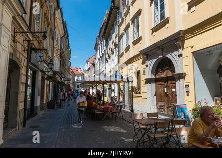 Café: In einer engen Straße in der Altstadt von Ljubljana, Slowenien, werden Tische, Stühle und Sonnenschirme im Restaurant serviert. Stockfoto