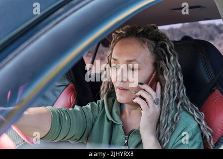 Schöne asiatische Frau mittleren Alters, die in einem Auto sitzt und am Telefon telefoniert. Stockfoto