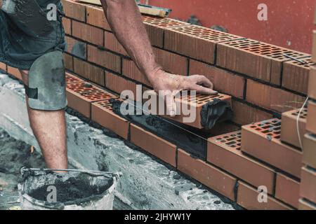 Arbeiter oder Maurer, die Ziegel legen. Baumeister macht auf der Baustelle Ziegelarbeiten, Nahaufnahme der Hände. Stockfoto