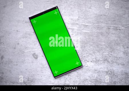 Das Smartphone verfügt über einen leeren grünen Bildschirm für Modelle wie App-Entwicklung Demo oder für den Einsatz im Grafikdesign. Handy liegt auf dem Tisch. Stockfoto