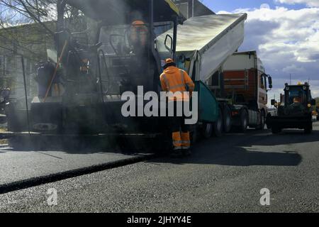 Straßenfertiger Arbeiter. Asphaltmaschine auf Straße Reparatur-Website. Erneuerungsprozess, Bauarbeiten. High-Angle-Ansicht Stockfoto