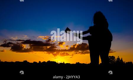 Ukrainisches Siegeskonzept, Silhouette einer Mutter mit einem Kind, das eine Flagge gegen einen blau-blauen Himmel hält. Stockfoto