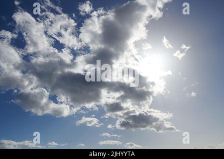Wolken. Sonne versteckt sich hinter Wolken mit blauem Himmel. Schöner Sonnenschein hinter weißen und grauen Cumulus-Wolken am Mittag im Sommer. Ruhige Aussicht auf Stockfoto