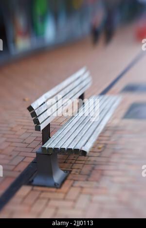 Landschaft aus leerer Straßenbank aus Holz. Isolierte und verwitterte öffentliche hölzerne Bank im Freien mit verschwommenem Hintergrund und Platz für Kopien auf einem Bürgersteig Stockfoto