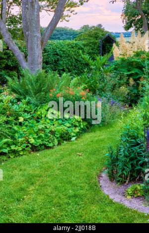 Lebendige, üppige grüne Natur in einem ruhigen Garten an einem sonnigen Tag. Viele Bäume, Sträucher und Blumen wachsen in ruhiger Harmonie. Beruhigende Aussicht von hell Stockfoto