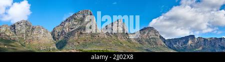 Twelve Apostles am Tafelberg in Kapstadt vor blauem Himmel von unten. Atemberaubende Aussicht auf Pflanzen und Sträucher, die um ein wachsen Stockfoto