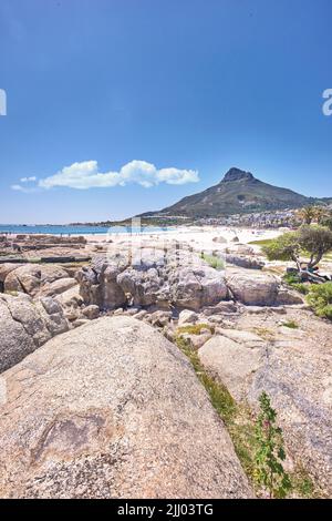 Große Felsen an einem Strand in der Nähe eines Berges mit einem blauen Himmel Hintergrund an einem heißen Sommertag. Die Landschaft eines felsigen Meeres oder Ozeanufers während der Frühlingsferien Stockfoto