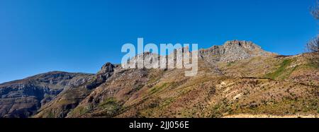 Twelve Apostles am Tafelberg in Kapstadt vor blauem Himmel von unten. Atemberaubende Aussicht auf Pflanzen und Sträucher, die um ein wachsen Stockfoto