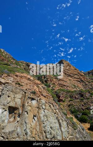 Landschaftlich reizvolle Berglandschaft vor blauem Himmel mit vereinzelten Wolken und Kopierraum von unten. Wilde Pflanzen und Sträucher wachsen auf felsigen Stockfoto