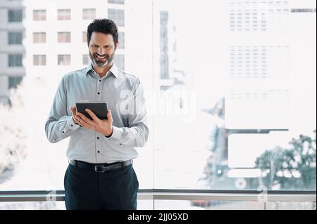 Auf Erfolg ausgerichtet. Ein reifer Geschäftsmann, der allein im Büro steht und ein digitales Tablet nutzt. Stockfoto