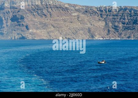 Santorini, Griechenland - 14. Mai 2021 : Blick auf ein kleines Fischerboot und die felsige vulkanische Landschaft von Santorini im Hintergrund Stockfoto