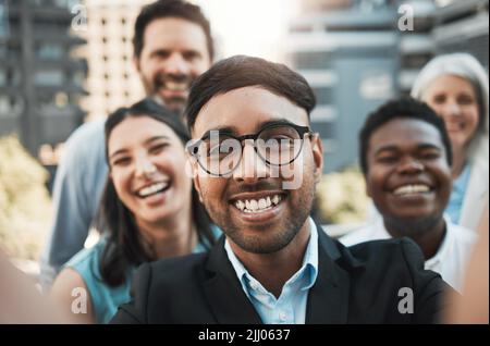 Sagen Sie Käse. Ein hübscher junger Geschäftsmann, der draußen mit seinen Kollegen steht und Selfies macht. Stockfoto