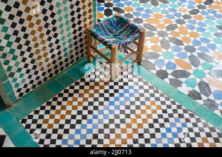 Blauer Stuhl aus Holz mit quadratischen Kachelmustern an der Wand und am Boden in einem wunderschönen Interieur in Marrakesch, Marokko Stockfoto