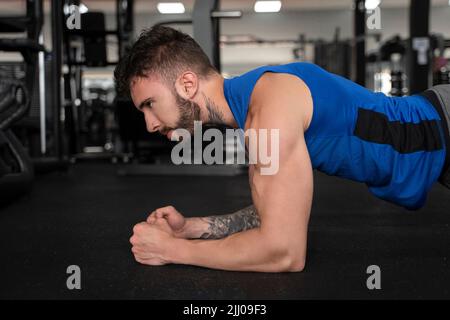 Schöner Mann mit Tattoos in seinem 20s tut Plank in der Turnhalle Stockfoto