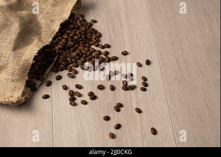 Kaffeebohnen, die aus einem hessischen Sack auf einem hellen Hintergrund auslaufen, würden den Hintergrund haben Stockfoto