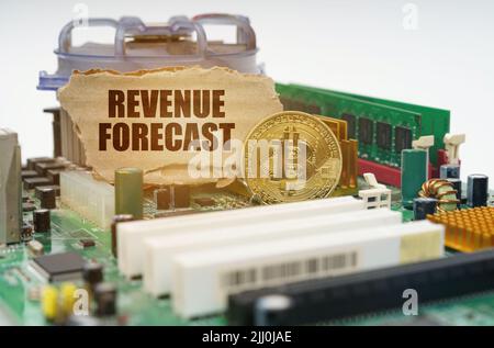 Krypto - Geschäftskonzept. Auf der Hauptplatine liegt eine Bitcoin-Münze und ein Pappschild mit der Aufschrift - Revenue Forecast Stockfoto