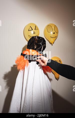 Kinder verkleiden sich, um Happy Halloween zu feiern. Weißer Geist in selbstgemachtem Kostüm aus Hauslaken und bemalt mit orangen Kugeln an der Wand. Festliches Design, Partykonzept. Feier zum Allerheiligen. Stockfoto