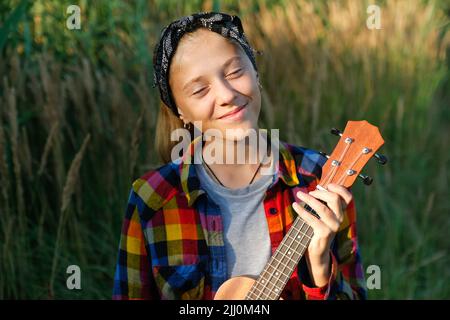 Defokussieren Mädchen mit Gitarre. Teen Mädchen zu Fuß auf Natur Hintergrund. Kleines Mädchen draußen. Grüne Wiese. Generation z. Herbst. Bandana. Lifestyle. Dre Stockfoto