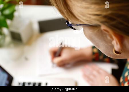 Defokussieren weiblicher Hand Schreibfeder. Unkenntlich elegante Frau, die im Büro am Computer arbeitet. Beginn oder Ende eines Arbeitstages. Arbeitsbereich. Draufsicht. Zeit Stockfoto