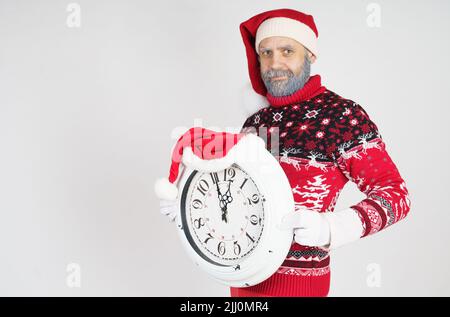 Weihnachts- und Weihnachtskonzept. Der Weihnachtsmann zeigt auf die Uhr vor Weihnachten. Weihnachtsmütze auf der Uhr Stockfoto