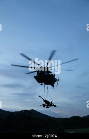 U.S. Marine Corps CH-53E Super Hengst mit Marine Medium Tiltrotor Squadron 262 (verstärkt), 31. MEU, hebt eine M777 geschleppte 155 mm Haubitze vom Boden während des Hubschrauberunterstützungsteams-Trainings in Camp Hansen, Okinawa, Japan, 19. Juli 2022. Die HST ermöglicht die Einrichtung einer zweckdienlichen Landezone für Flugzeuge und ist in der Lage, Ausrüstung wie Joint Light Tactical Vehicles und Haubitzen für die Abholung zu sichern. Die 31. MEU, die einzige kontinuierlich im Vorwärtslauf eingesetzte MEU des Marine Corps, stellt eine flexible und tödliche Streitmacht bereit, die als Erstkrisen bzw. Stockfoto