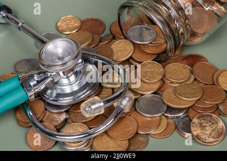 Das Konzept von Wirtschaft und Medizin kostet Gesundheit. Stapel von echten Münzen und Stethoskop. Wirtschaftliche Gesundheit isoliert auf grünem Hintergrund. Stockfoto