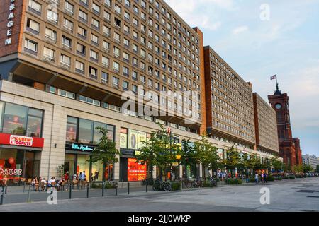 Blick auf die Außenfassade des Rathauspassagen im Sommer am Alexanderplatz mit rotem Rathaus und Wolken im blauen Himmel im Hintergrund. Stockfoto