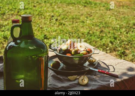 Eine große Flasche Obstmost auf rustikalem Tisch mit Birnenernte, an einem Herbsttag Stockfoto