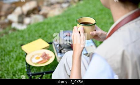 Beschnittene und Nahaufnahme Hände Bild, glücklich und entspannt asiatische weibliche Camper hält eine heiße Kaffeetasse, nippen Morgenkaffee während Camping auf dem Campgrou Stockfoto