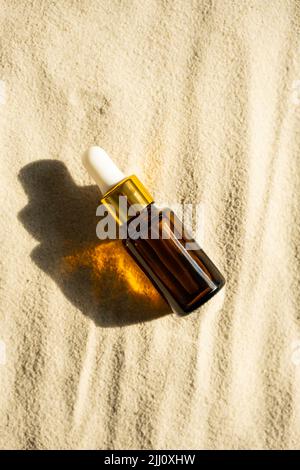 Imitierte Serumflasche aus bernsteinfarbenem Glas auf Sandhintergrund. Pipetten-Gesichtskosmetik im Sonnenlicht, minimalistischer Trend. Stockfoto