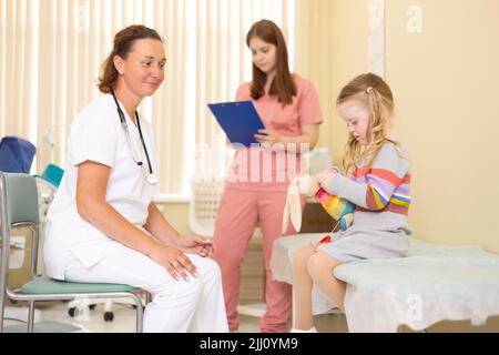 Arzt und Krankenschwester unterhalten sich mit einem kleinen Mädchen im Arztbüro Stockfoto