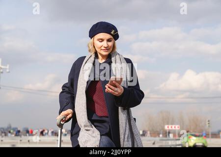 Eine Frau in der Stadt mit einem Koffer nutzt ein Smartphone. Stockfoto