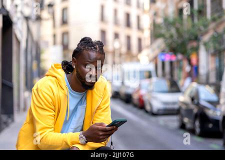 Junger afrikanischer Mann, der sein Smartphone in der Stadt konsultiert Stockfoto