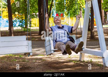 Verspielte und glückliche ältere Frau genießen bei Schaukel im Freien in Park oder Garten entspannt, fröhlich aktiven Ruhestand und Entspannungskonzept. Großeltern Tag Stockfoto