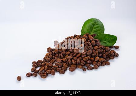 Gruppe von Kaffeebohnen mit grünen Blättern. Kaffeesorten und Blätter auf weißem Hintergrund mit Kopierfläche. Stockfoto