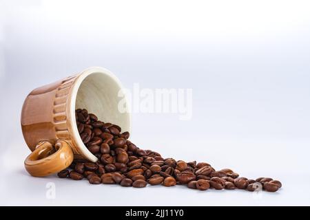 Geröstete Kaffeebohnen verschüttet aus Kaffeebecher umgedreht auf weißem Hintergrund mit Kopieplatz. Selektiver Fokus, Karte für Café, Café, Konditor Stockfoto