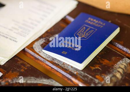 Details zur geringen Schärfentiefe (selektiver Fokus) mit einem verschlissenen biometrischen ukrainischen Pass neben offiziellen Ausweispapieren auf einem Holztisch. Stockfoto