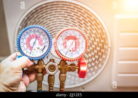 Luftreparaturmechaniker mit Messgeräten zum Befüllen von industriellen Klimaanlagen und zur Überprüfung der Wartung der Außenluftkompressoreinheit. Stockfoto