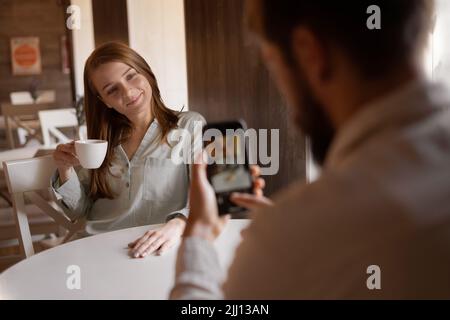 Verliebtes Paar, das im Café sitzt, fotografierter Fotograf mit einer Tasse Kaffee Frau auf dem mobilen Smartphone, mobile Innenfotografie, Social Me Stockfoto