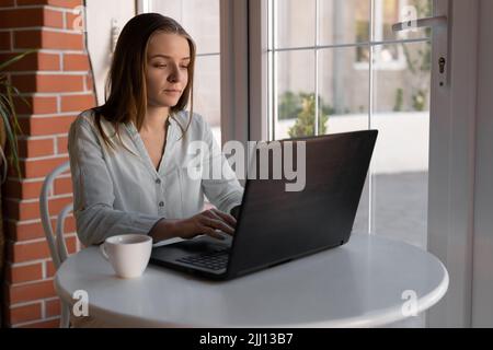 Schönes junges Mädchen, das in einem Café mit einem Laptop arbeitet, freiberufliche Fernarbeit, blonde Studentin arbeitet nach ihren Vorlesungen am Notebook Stockfoto