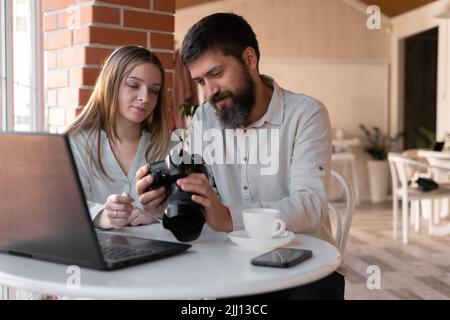 Junge, erfolgreiche freiberufliche Fotografin, die während der Arbeit im Café Bilder vor der Kamera durchschaut. Neues Konzept moderner Technologien Stockfoto